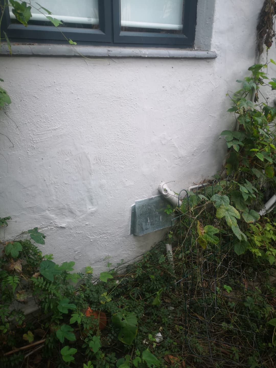 Vent cover fitted below a window, shielded from the weather